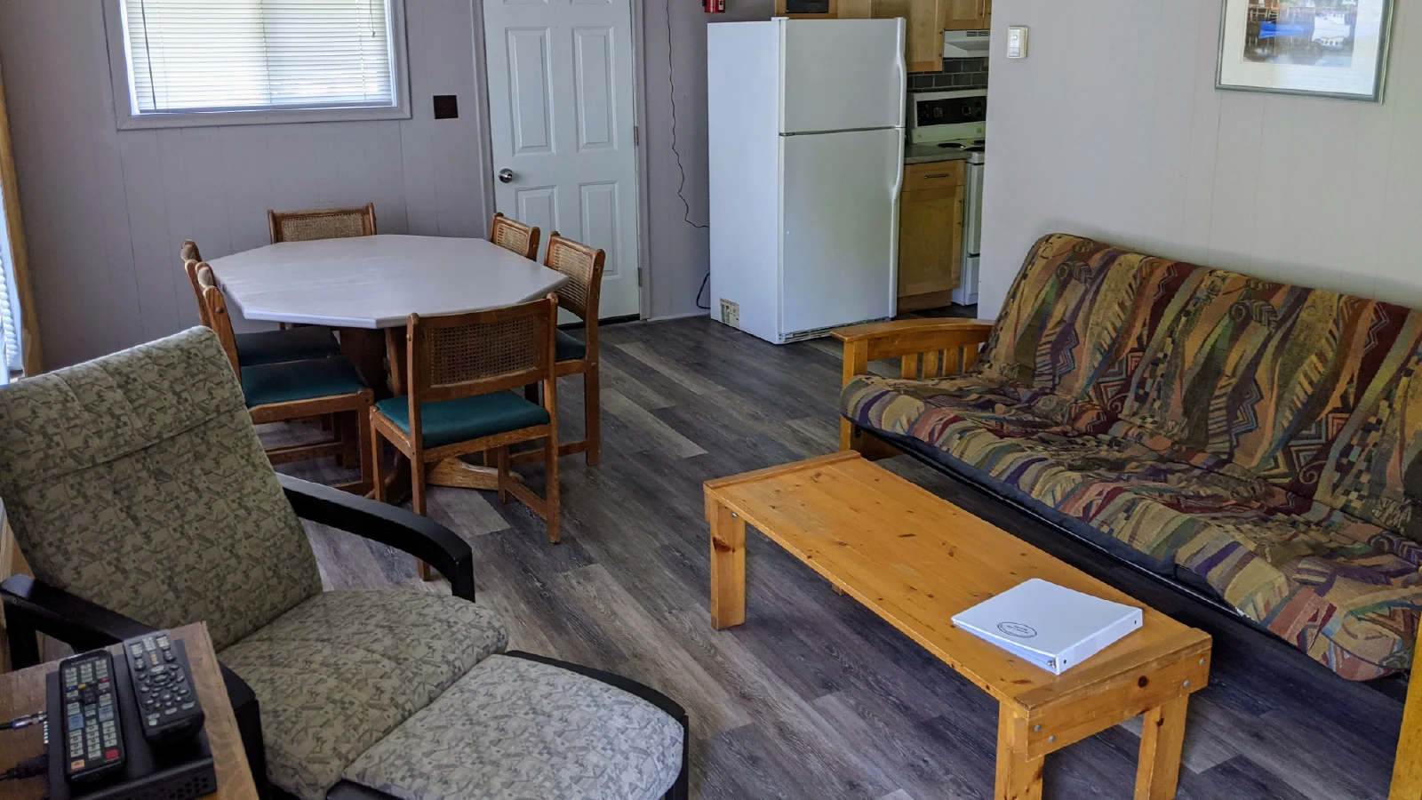 Pigeon Lake Resort Cottage 8.&nbsp; Open-concept living area with dining table, sofa, armchair, coffee table, and kitchen with refrigerator.